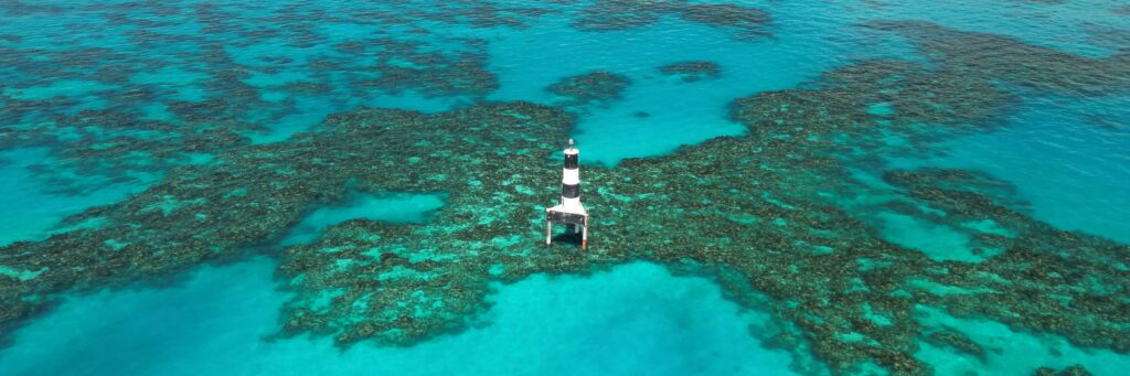 A black and white striped lighthouse stands in the middle of turquoise blue water, surrounded by coral reefs—a stunning scene that ranks high among Bermuda must see attractions.