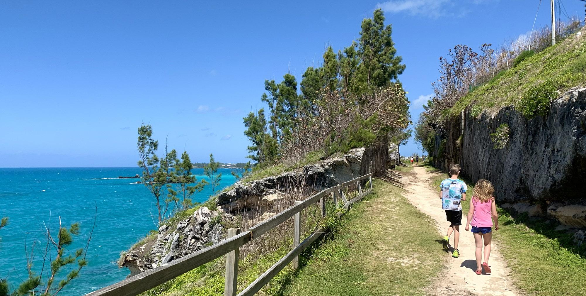 People walking along a scenic coastal path, surrounded by lush green vegetation and enjoying breathtaking views of the turquoise ocean. This picturesque setting showcases the beautiful weather in Bermuda, ideal for outdoor activities and exploration.