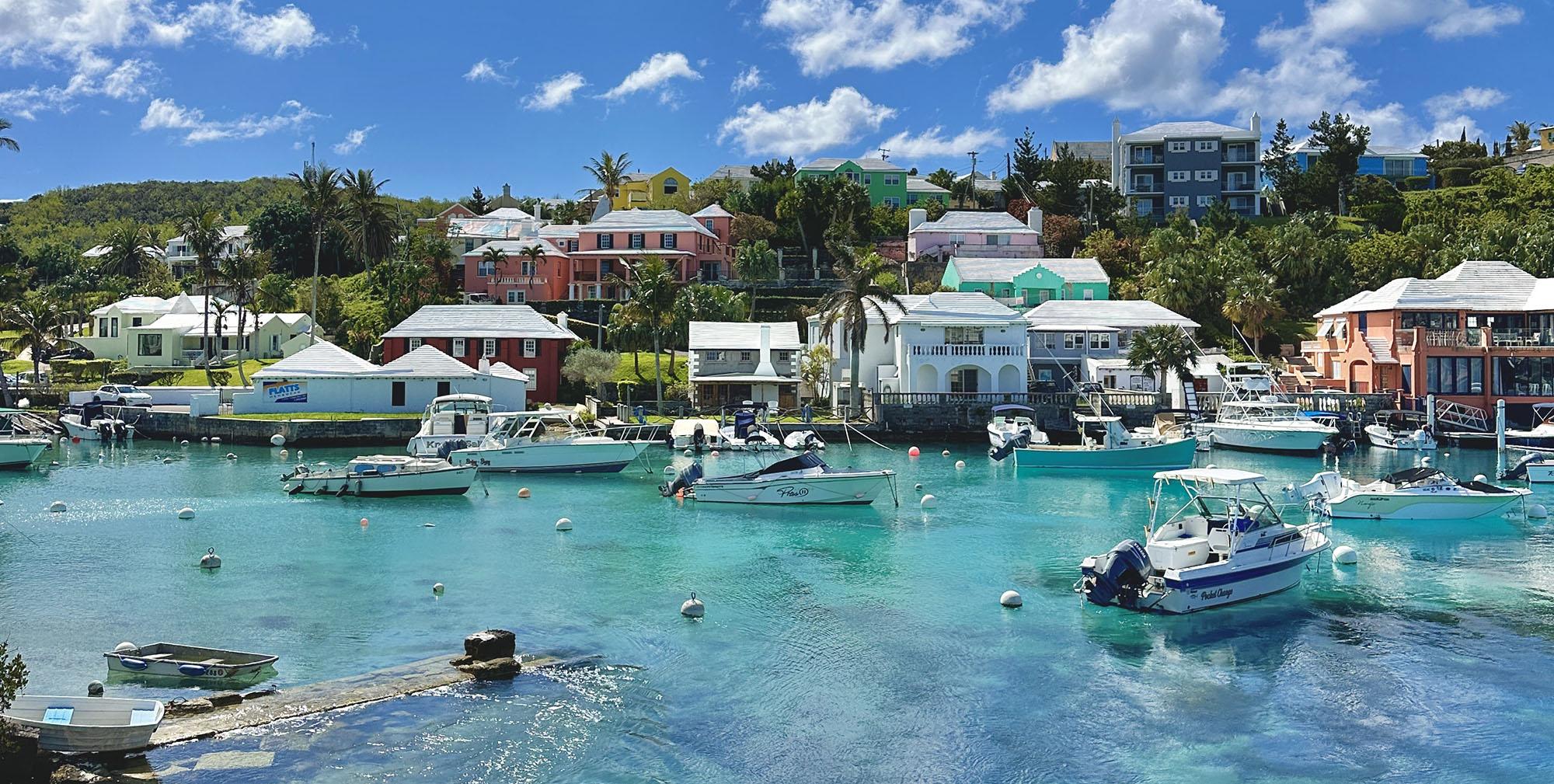 The image depicts a traditional Bermuda cottage characterized by its distinctive white stepped roof, designed for rainwater collection, set against the backdrop of the island's natural beauty. This architectural style reflects Bermuda's historical significance as a British overseas territory in the Atlantic Ocean, known for its unique charm and vibrant culture.