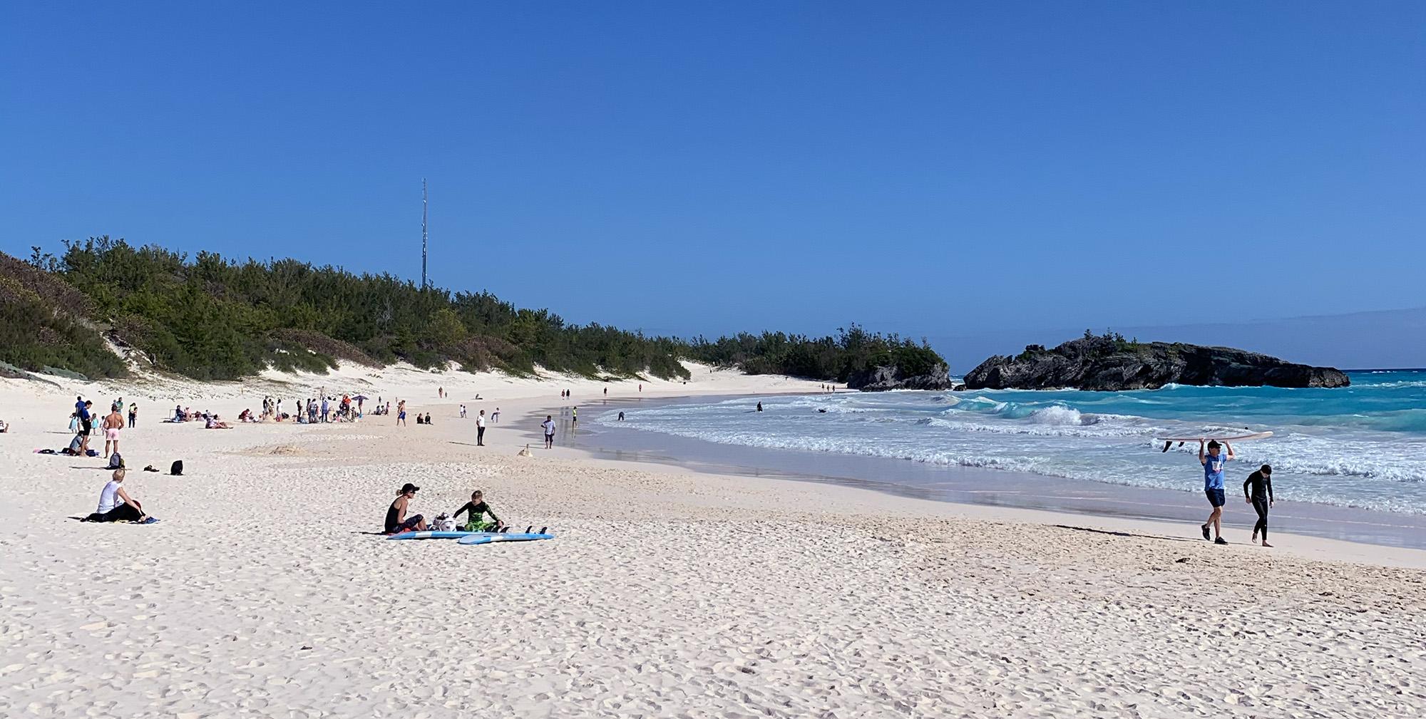 The image showcases the stunning Horseshoe Bay pink sand beach with gentle turquoise waves lapping against the shore, framed by unique limestone rock formations. This picturesque scene embodies the natural beauty of Bermuda, a popular destination in the Atlantic Ocean known for its exquisite pink sand beaches and rich historical significance.